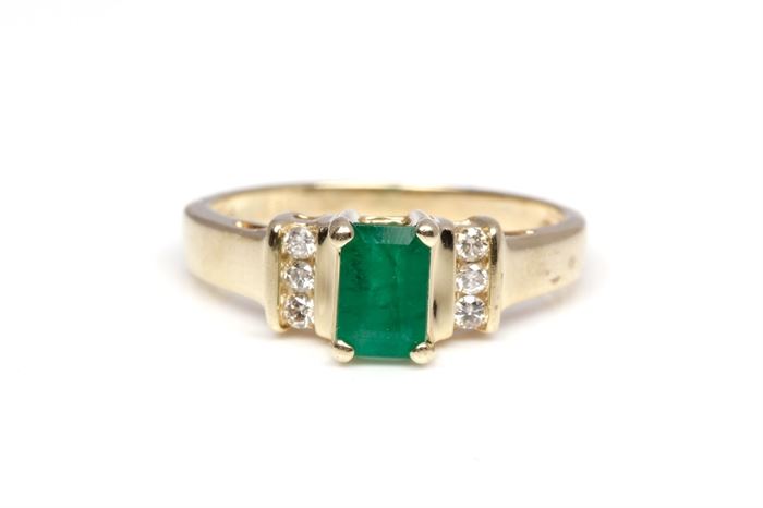 14K Yellow Gold Emerald and Diamond Ring: A yellow gold shank with a basket prong set emerald to he center and bar set round cut diamonds to the shoulders.