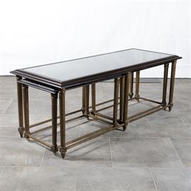 Set of Three Gold Tone and Black Painted Nesting Tables: A collection of nesting tables painted in black and gold tone enamel. These tables include a large table with an oversized top with beveled frame enclosing an inset panel of wicker under glass over turned and fluted legs ending in peg feet with stretchers between for support. Also included is a pair of smaller tables which are sized to slide underneath the ends of the larger table and include a louvered slat shutter style top enclosed by a beveled frame and resting on turned and fluted legs ending in peg and caster feet with stretchers for support.