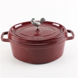 Staub Cocotte With Rooster: A Staub cocotte. This dark red cast iron dutch oven, or cocotte, features a silver tone rooster finial at the center of its cast iron lid. The lid is marked “Staub” and “La Cocotte”.