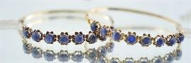 Lot 39: Antique pair of matching blue sapphire bangles in 18kt yellow gold set with sixteen, 5.5 mm dark (some grayish) violet-ish blue cabochons approx. 13-16 ct tw, 7”, 27 grams