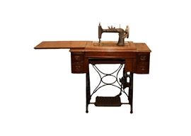 Vintage New Home Ruby Treadle Sewing Machine: A vintage Ruby treadle sewing machine set in its original decorative oak wood cabinet, featuring a black cast iron frame, treadle, and wheel, two pull out drawers on either side and a pull-up extension that easily raises and lowers the sewing machine.