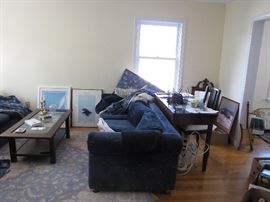 A deconstructed living room with oriental-style rug, desk with matching chair, sofa table and two blue sofas plus