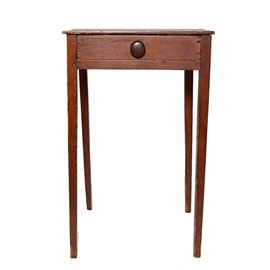 Antique Pine One Drawer Stand: An antique pine end table. Featuring a dark brown stain, this table features a single drawer with a circular drawer pull at the center. The table stands on square legs and is unmarked.