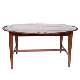 Antique Butlers Table: An antique mahogany butler’s table. This antique mahogany butler’s table with hinged sides to use either up making the table rectangular or down making the table oval. The coffee table has a parquetry top, cut out handles at each side and square tapered legs with a “T” stretcher.