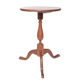 Pedestal Side Table: A pedestal side table. This wood side table presented in a chestnut finish features a round table surface. The table surface rests on a turned pedestal base which meets three splayed legs.