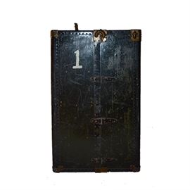 Vintage Wardrobe Trunk by Hartmann: A vintage wardrobe trunk by Hartmann. This rectangular piece with black finish and brass tone hardware opens to five stacked drawers with bail handles and a second compartment with wooden hangers. This piece is marked “Hartmann Cushion Top Wardrobe Trunks” and features additional labels and markings throughout.