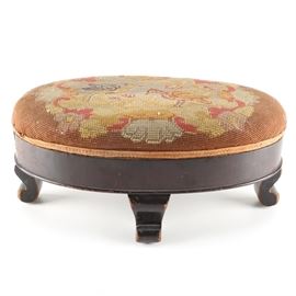 Antique Ogee Stool With Needlepoint Detailing: An antique ogee stool with needlepoint detailing. This stool features a needlepoint stitching on the top that depicts two doves surrounded by a floral setting. The base is wooden with a mahogany stain and ogee legs. The stool is marked “Kittinger Furniture Buffalo Worth While 1866.”