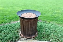 Outdoor Gas Fire Pit with Decorative Center Stones: A contemporary, gas fire pit featuring a bamboo-like structure to its exterior and a metal bowl at the top filled with decorative, pink stones that sit in the center where the flames burn. It has a manual gas burner, which is accessed from the side.