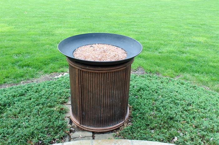Outdoor Gas Fire Pit with Decorative Center Stones: A contemporary, gas fire pit featuring a bamboo-like structure to its exterior and a metal bowl at the top filled with decorative, pink stones that sit in the center where the flames burn. It has a manual gas burner, which is accessed from the side.