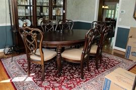 Stanley Furniture Dining Table: A Stanley Furniture dining table and chairs. This oval wooden table features two removable leafs and cover padding. There are six chairs included with matching wood stained frames and beige and black patterned upholstery.