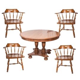 Ethan Allen Wood Dining Table and Chairs: An Ethan Allen wood dining table and chairs. Featured here is a four foot round dining table that becomes oval when the leaves are added. The base of the table splits in half, dividing the two legs and the bottom pedestal with four bun feet into two sections that support the oval table. Hidden on the underside of the pedestal between the bun feet are two metal casters and there is a metal ring attached to the base for separating the two sections. Also included are four dining chairs with arms and spindle backs. All of this furniture is made from a warm toned brown polished wood.