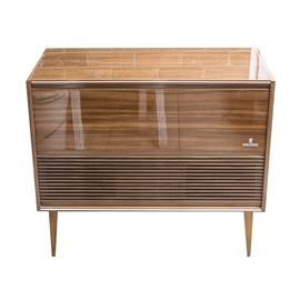 Grundig Mid-Century Stereo Cabinet: A mid-century Grundig stereo cabinet with record player, model KS 737 U. The cabinet dates to the 1950s or ‘60s. The rectangular cabinet has clean, straight lines, with horizontal ribs across the speaker on the front. The cabinet is made a highly polished wood and is labeled “Grundig” to the front. The cabinet rests on square, tapered legs. The top of the cabinet is hinged and lifts up to reveal a record player and space for records. The record player is marked “Grundig Automatic 36”, and has settings for playing various sized records including 78s, 45s and more. Included with the stereo cabinet is a collection of vintage vinyl records. Also includes the original owner’s manual.