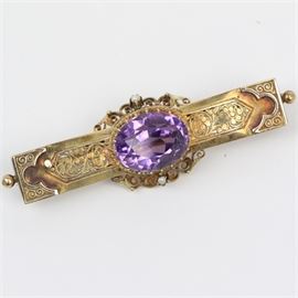 Victorian 14K Yellow Gold, 9.50 CTS Amethyst, and Seed Pearl Filigree Bar Brooch: A Victorian 14K yellow gold filigree brooch featuring one center faceted oval amethyst with a braided border and two seed pearls mounted against a delicate filigree frame with a c-clasp closure.