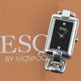 Movado ESQ Stainless Steel and Diamond Women's Wristwatch: A stainless steel Movado ESQ women’s wristwatch featuring a rectangular case with two diamonds mounted in a black dial and a stainless steel bracelet and foldover clasp. Item is untested and presents in its original box with manual and warranty card.