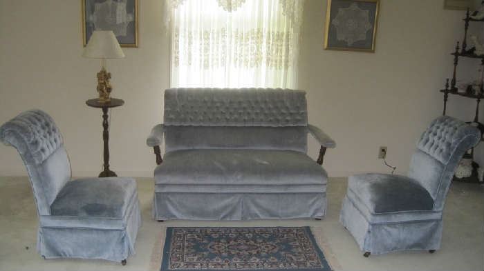 Sitting area with powder blue upholstered tufted love seat and two occasional chairs, candlestick table on left side