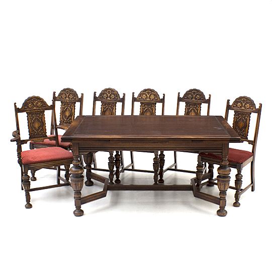 Vintage Jacobean Style Oak Dining Table and Chairs: A vintage Jacobean style oak dining table and chairs. It features extendable leaves with an incised border and sits on turned legs with bun style feet. The chairs feature a shallow relief carved crest with a floral motif, as well as, a carved back splat. They sit on turned legs with bun style feet, and are covered with red upholstery. For matching dining room furniture, see 17CIN216-490 and 17CIN216-462.