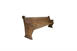 Wooden Church Pew: A wooden church pew. The pew features a bench seat, carved scroll accents on the arms, and pointed-arch window shape carved into either side. The back has a wooden pocket to hold bibles.