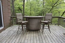 Outdoor Semi-Circular Bar and Counter Height Armchairs by Castelle: An outdoor semi-circular bar and pair of counter height armchairs by Castelle. The bar features a chevron style slatted wood-look metal top, a brown woven vinyl front, two fixed shelves, and a metal frame support/footrest with squared legs at the base. The tall armchairs have dark copper tone metal frames and woven seats matching the bar. Companion 17BAL049-041.