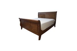 King Size Sleigh Bed Frame: A king size sleigh bed frame. The dark oak headboard and footboard each feature decorative carvings depicting a rope design over rectangular panels and scrolled sides embellished with bullseye medallions. Both pieces stand on short saber legs and are supported in place with wooden rails. Please note the mattress is not included. This item will require tools to disassemble and is located on the second floor.
