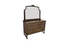 Antique Dresser With Attached Mirror: An antique dresser with an attached mirror. The dresser features: a rectangular overhanging top, three partial length drawers over two full length drawers, decorative carving on the skirt, and turned ball feet on platform bases with casters. An ornate carved medallion in the front center, decorative molding on the drawers, and ornate metal plates around the wood knobs accent the piece. A removable mirror with a decorative floral acanthus carving and turned finials is attached to the back. This item is located on the second floor.