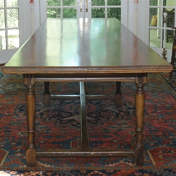 Handcrafted Walnut Harvest Table: A handcrafted walnut harvest table. This piece features a rectangular surface with a scroll pattern stenciled in stain to its border. The table has an apron with vase turned blocks above its six turned legs, connected by stretchers.