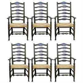 Vintage Oak Rush Seat Ladder Back Armchairs: A set of six vintage oak ladder back armchairs with rush seats. Each chair features six arched top wrung support slats leading to rounded finials, a square rush seat, and turned ring spindle legs with turned spindle stretchers supporting the piece. The chairs are unmarked.