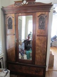 Antique armoire with walnut veneer and intricate carving.  Clothing racks inside and storage drawer below.