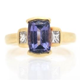 18K Yellow Gold Tanzanite and Diamond Ring: An 18K yellow gold tanzanite and diamond ring. This features a center emerald cut tanzanite stone with two princess cut diamonds on either side of the shoulders.