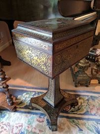 English Regency period coffer-form tea caddy on stand (or teapoy), hinged top above four canisters with brass scrollwork decorated (or Boulle-work) lids, quatrefoil base with casters.
