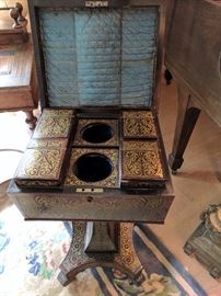 English Regency period coffer-form tea caddy on stand (or teapoy), hinged top above four canisters with brass scrollwork decorated (or Boulle-work) lids, quatrefoil base with casters.
