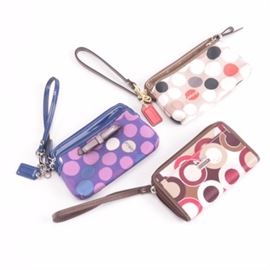 Coach Wristlets: A collection of Coach wristlets. Included is the Madison Graphic Op Art Universal case and the Madison Graphic Op Art Universal case. The pieces are each marked “Coach” across the front with several interior pockets and a zipper closure.
