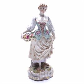 Reproduction Meissen Porcelain Female Sculpture: A reproduction Meissen porcelain sculpture. This piece depicts a barefoot young woman in a Bavarian style dirndl dress with a floral pattern. The woman is carrying a basket of multicolored roses, resting at her right hip. There is gilt detailing to the dress corset and scrolled base. The underside is stamped with a reproduction Meissen crossed swords mark.