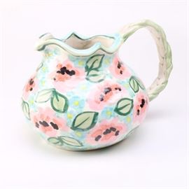 Hand-Painted Ceramic Pitcher: A hand-painted pottery pitcher. This piece features a scalloped rim with hand-painted floral and leaf patterns as well as a braided rim. The underside reads, “Dagma”.