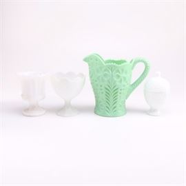 Assorted Milk Glass Vases, Dish and Jadeite Pitcher: An assortment of milk glass vases, lidded dish, and jadeite pitcher. This assortment features a green jadeite pitcher with a floral relief design and scalloped rim. Also included is a pair of milk glass pedestal vases with scalloped rims and a 1960’s Avon egg shaped lidded milk glass candy dish.