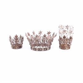 Metal Crowns: A collection of metal crowns. Included are three crowns with floral and star patterns and embellishments throughout. It has a slit design across each crown with an open design. Several of the pieces offer clear stones adornments throughout. A sticker to the inside of one crown reads “Made in India”.