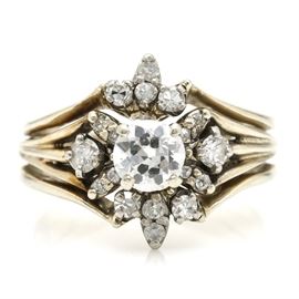 14K White Gold 1.02 CTW Diamond Ring: A 14K white gold 1.02 ctw diamond ring. This ring features a central prong set, peg head diamond surrounded by a radiating abstract motif made from prong set diamond clusters. The flared shoulders are split and taper together at the shank.