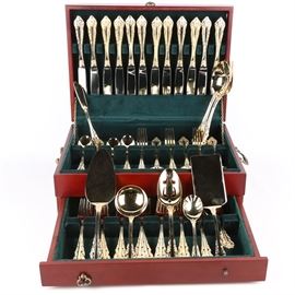 Wallace "Antique Baroque" Gold Plate Flatware Service for Twelve: A set of Wallace Silversmiths 24K yellow gold electroplated flatware. The flatware was made by Wallace and is in the “Antique Baroque” pattern. The set contains twelve each of the following: knives, dinner forks, salad forks, teaspoons, and tablespoons. Also included is a pierced serving spoon, sugar shell, sauce spoon, casserole spoon, pie server, lasagna server, and master butter knife. All are housed in wooden storage case.