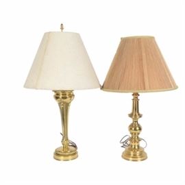 Two Classic Brass Lamps, Including Stiffel: A set of two brass table lamps. The pair includes a Stiffel brass lamp featuring a classic round, turned brass column and base. It is topped with a round, flared jute string shade, which is fully lined in a silky fabric, with gold tone fabric trim around the top and bottom edges. This lamp is marked “Stiffel” to the socket, which takes a single standard bulb, with a knob switch on the side of the socket. A slightly taller table lamp with a round base and narrow, tapered column features alternating smooth and textured vertical bands, with a round brass base. This lamp is topped with a windowpane-textured white fabric shade, and takes a single standard bulb. The lamp switches on at the socket, and is not marked.