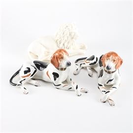 Figurines of a Lion and Two Dogs Featuring Chelsea House: A collection of three animal figurines. This includes a pair of dogs with brown and black patches throughout hand made in Italy by artist Chelsea House. The third is a lion in a matte off-white ceramic.