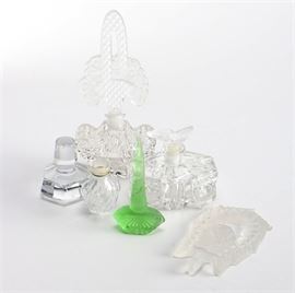 Selection of Decorative Cut Glass: A selection of decorative cut glass. This selection includes a frosted glass stopper with a rose design; a green glass piece with a palmette style base; and a stopper with cut corners. Also included is a small glass bottle marked “Bottle Made by Alioue”; a perfume bottle with cut corners and has star cut designs; and perfume bottle with a decorative stopper.