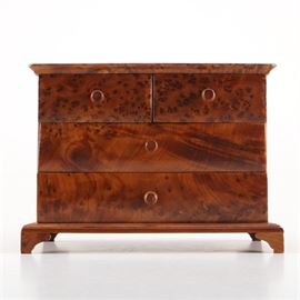 Brown Wooden Jewelry Chest: A brown wooden jewelry chest. This rectangular storage unit is made of thuya wood and features four drawers with simple pull knobs and sits on bracket feet. A Saks Fifth Avenue decal is present to the underside of the chest.