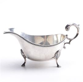 Circa 1910 William Hutton & Sons Ltd Sterling Gravy Boat: A sterling silver gravy boat by William Hutton & Sons Ltd circa 1910. This piece features a spout with a gadrooned edge and a scroll handle as well as foliate knees and hoof feet. English hallmarks are present next to the handle. The approximate weight is 3.860 ozt.