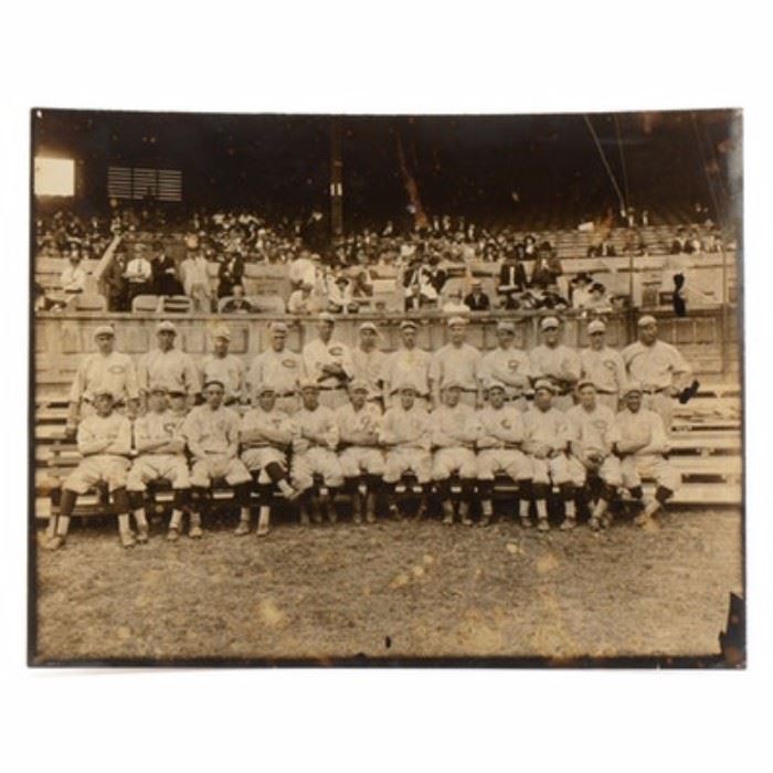 Original 1919 Reds Photo: An original first generation 1919 Cincinnati Reds team photo. The photographer’s stamp is on the back, “J. R. Schmidt 1557 St. Charles Place, Hyde Park Cincinnati, O”. There is a written notation on the back, done in black fountain pen that has the first and last names of the players and “Official Group Penant Winning Reds”. The players are in uniform, sitting on some wood bleachers on the field. The stands behind the players has fans arriving for the game. The photo is not dated per se, but the notation stating that it’s the “Penant Winning Reds” dates it, as the Reds only pennant win of this era was in 1919. The names listed (as they are written on the back) are: “Back Row – Sherwood Magee, Eddie Roush, Morris Rath, Hod Eller, Harry Sallee, Eddie Gerner, Ray Fisher, Jimmy Ring, Heinie Groh, Rube Bressler, Hank Schreiber and Roy Mitchell Front Row – Jake Daubert, Charley See, Walter Ruether, Pat Moran, Bill Rariden, Nick Allen, Ivy Wingo, Greasy Neale, Pat Du