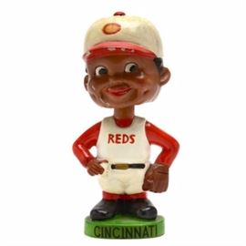 1962 African-American Reds Bobblehead: A 1962 Cincinnati Reds African-American bobblehead. This little guy was made in Japan, the bottom is marked with the year and maker. He’s dressed in the early 1960s uniform, he’s holding a baseball in one hand and has his glove on the other hand. “REDS” is embossed on the front of the jersey; “CINCINNATI” is in black lettering on the front of the green round base. The “C” on the front of his white hat is a decal. The bobblehead is made of a chalk/plaster material.