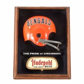 Bengals and Hudepohl Beer Ad: A vintage 1977 Cincinnati Bengals Hudepohl Beer football sign is featured. This classic sign is made of a durable molded plastic with a replica NFL “old style” Bengals football helmet protruding from its center. The sign also has a vintage Hudepohl Beer advertisement that reads “The Pride Of Cincinnati.” This mid-century advertising sign retains its bold colors and has a black cardboard backing. A small paper label is affixed to the back of the sign, it says, “© 1977 Embosograph Display Mfg. Co. Chicago, Illinois 60614”.