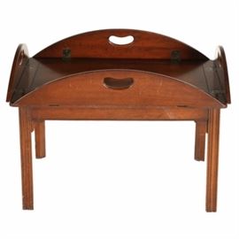 Mid 20th Century Mahogany Tray Table: A mid 20th century tray table made in mahogany with hinged sides which have cut-out handles and fold down to form an oval table top if desired. The top tray is not attached to the base which has straight reeded legs. Stamped “1075” and “E780” to the under side of the base.