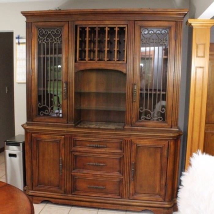 Walnut Stained China Cabinet and Buffet: A walnut stained wooden china cabinet and buffet combination. This large piece features a top section with a wine rack over two glass shelves, flanked by cabinets with shelves behind their glass paned doors with curl and rod wooden overlay. The bottom portion has three center drawers with a cabinet on each side. It has beveled molding to the crown, center, and base.
