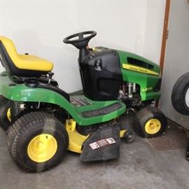 LA105 John Deere Tractor 100 Series and Trailer: A LA105 John Deere tractor 100 Series and accompanied trailer. The John Deere mower is a riding mower and part of the 100 series. It is accompanied by a 10p trailer which attaches to the back.