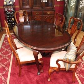 Queen Anne Style Extendable Dining Table and Chairs by Broyhill: A Broyhill Queen Anne style leaf dining table and chairs. This oval table is in a smooth dark cherry finish with cabriole legs and pad feet, and includes one extension leaf. There are six dining chairs included. Each identical chair features a light cherry wood finish and a beige patterned upholstery, with double yoke crestrails, shell accented fiddle back splats, cabriole legs, and pad feet; two have curved armrests.