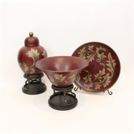 Ceramic Decor Collection: A collection of ceramic decor. All painted in a brick red with beige floral motif, this includes an urn which sits atop a resin stand, a vase which also sits atop a resin stand, and a decorative plate accompanied by an iron stand.